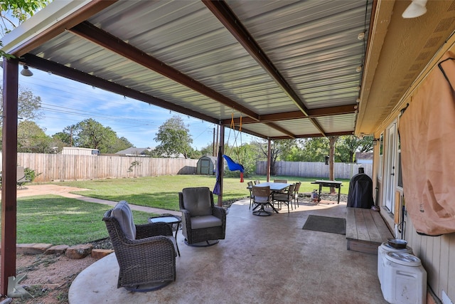 view of patio / terrace with a fenced backyard, a storage unit, outdoor dining area, and an outbuilding