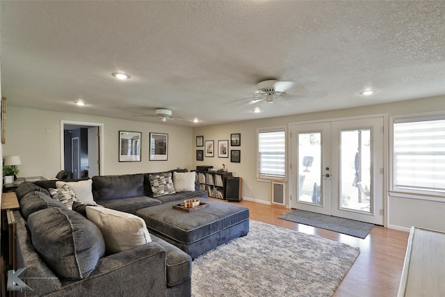 living area with a ceiling fan, french doors, light wood-style flooring, and a textured ceiling