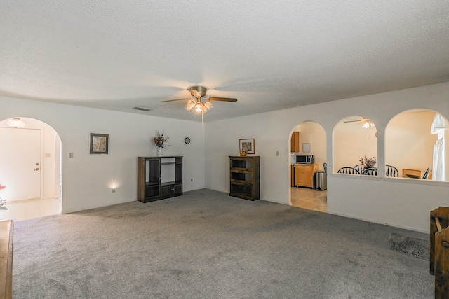 unfurnished living room with light carpet, ceiling fan, and a textured ceiling