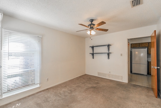 empty room with carpet flooring, ceiling fan, and a textured ceiling