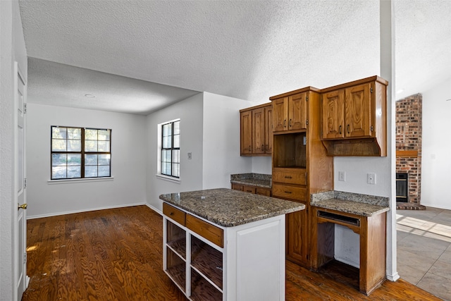 kitchen featuring a textured ceiling, a fireplace, dark stone countertops, and dark wood-type flooring