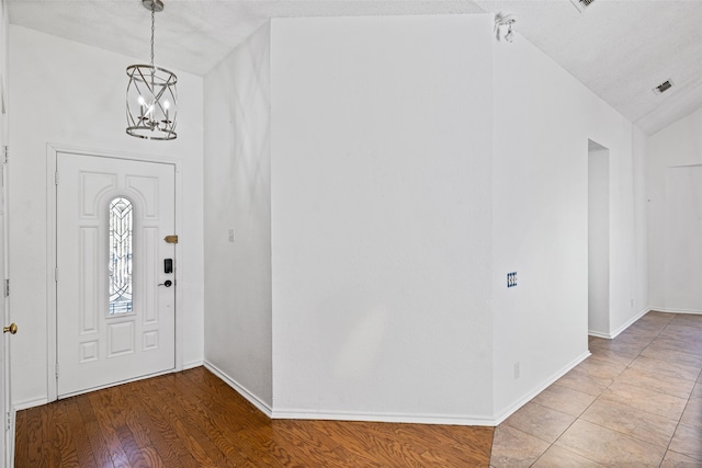 foyer entrance with a textured ceiling, wood-type flooring, lofted ceiling, and a notable chandelier