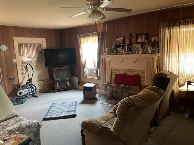 carpeted living room with ceiling fan, a fireplace, and wood walls