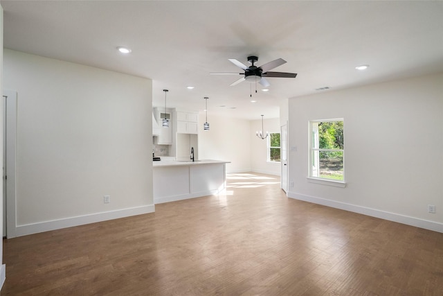 unfurnished living room with hardwood / wood-style floors, ceiling fan with notable chandelier, and sink