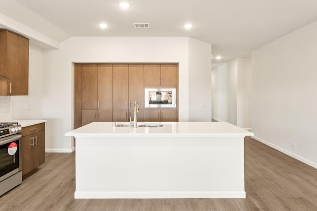 kitchen with brown cabinetry, gas stove, a sink, and built in microwave