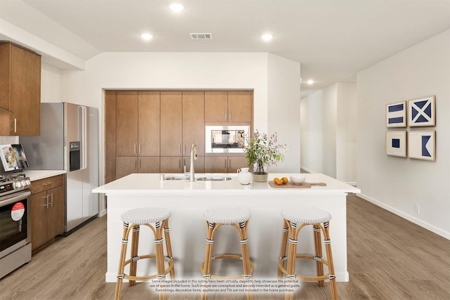 kitchen featuring stainless steel appliances, a sink, a kitchen breakfast bar, light wood finished floors, and brown cabinetry