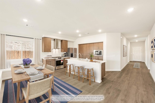 kitchen with a center island with sink, stainless steel appliances, light countertops, visible vents, and wall chimney exhaust hood