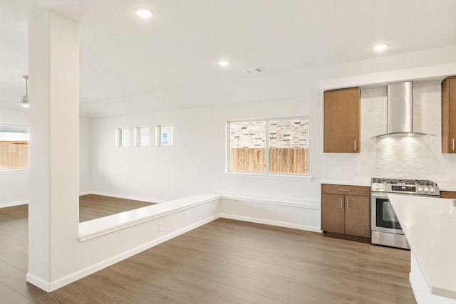 kitchen featuring stainless steel gas range oven, wood finished floors, light countertops, wall chimney range hood, and decorative backsplash