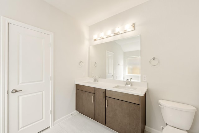 bathroom featuring double vanity, a sink, toilet, and baseboards