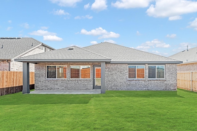 back of house with brick siding, a lawn, a fenced backyard, and roof with shingles