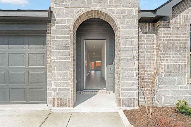 doorway to property with a garage, stone siding, and brick siding