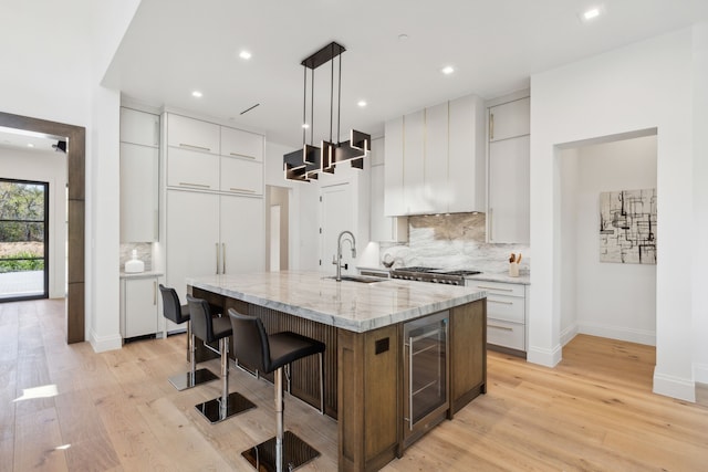 kitchen featuring white cabinetry, sink, hanging light fixtures, wine cooler, and a kitchen island with sink