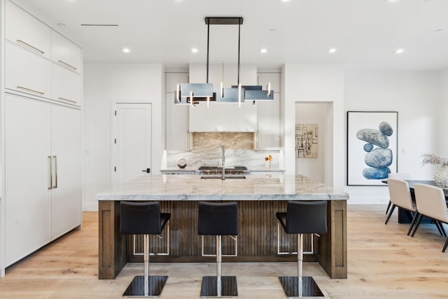 kitchen with a breakfast bar area, a kitchen island with sink, light hardwood / wood-style flooring, and pendant lighting