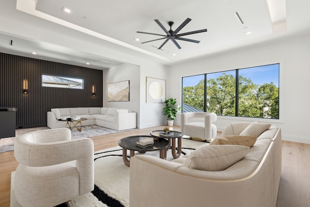 living room with ceiling fan, light hardwood / wood-style floors, and a raised ceiling