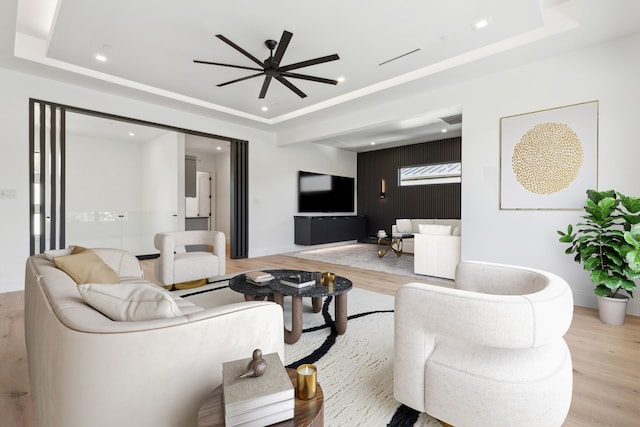 living room featuring a raised ceiling, ceiling fan, and light hardwood / wood-style floors