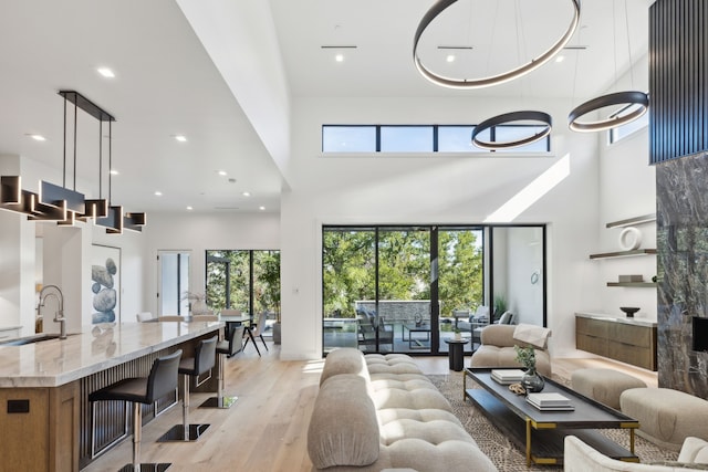 living room featuring plenty of natural light, a towering ceiling, light hardwood / wood-style floors, and sink