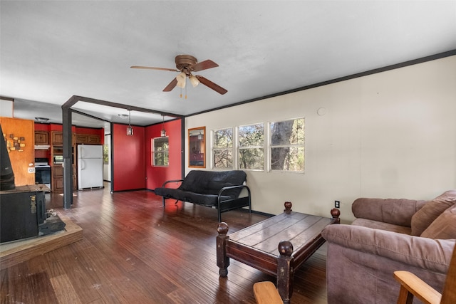 living room featuring ornamental molding, a wood stove, ceiling fan, and dark wood-type flooring