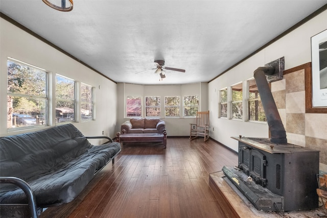 living room with dark hardwood / wood-style floors, a wood stove, ceiling fan, and crown molding