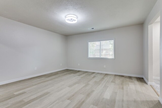 unfurnished room with light wood-type flooring and a textured ceiling