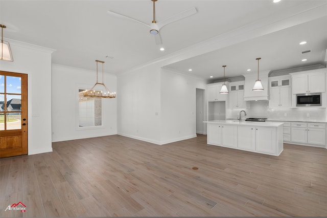 kitchen with white cabinetry, stainless steel microwave, light hardwood / wood-style flooring, an island with sink, and pendant lighting