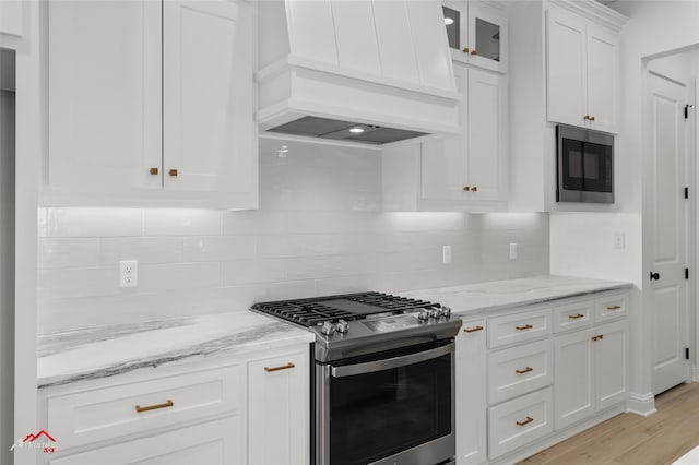 kitchen with light wood-type flooring, premium range hood, light stone counters, stainless steel appliances, and white cabinets