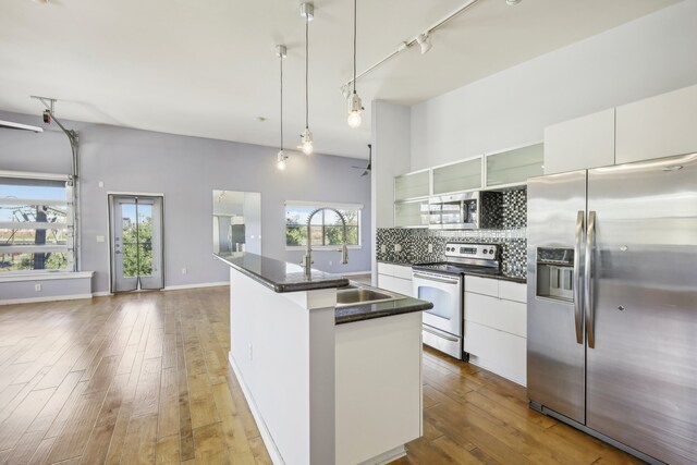 kitchen featuring dark hardwood / wood-style flooring, stainless steel appliances, decorative light fixtures, white cabinetry, and an island with sink