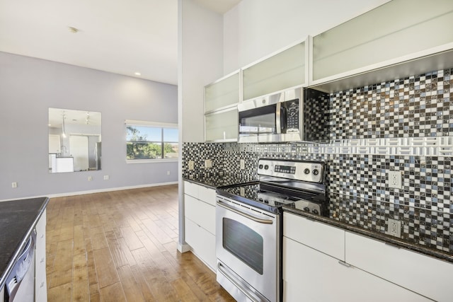 kitchen with appliances with stainless steel finishes, tasteful backsplash, dark stone counters, light hardwood / wood-style floors, and white cabinetry