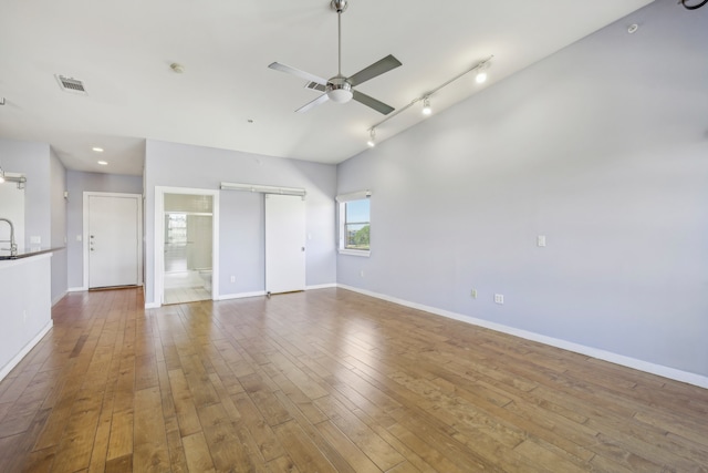 empty room with a barn door, hardwood / wood-style flooring, track lighting, and ceiling fan