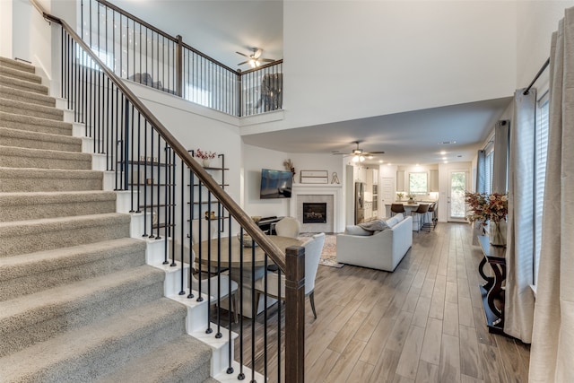 staircase with wood-type flooring, a towering ceiling, and a tiled fireplace