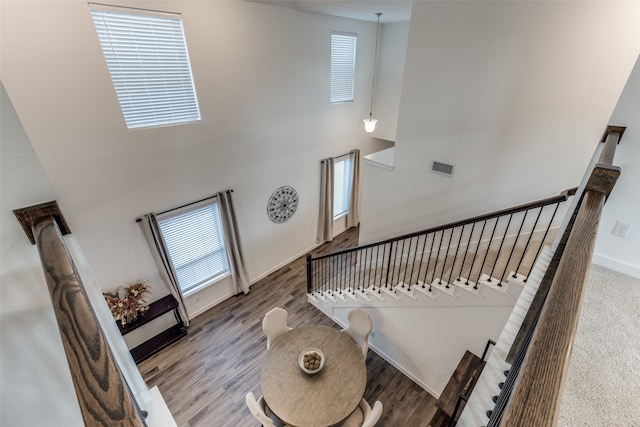 staircase with a high ceiling, a healthy amount of sunlight, and hardwood / wood-style floors