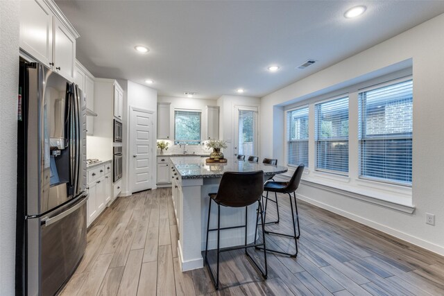 kitchen with light wood-type flooring, stainless steel appliances, a healthy amount of sunlight, white cabinets, and a kitchen island