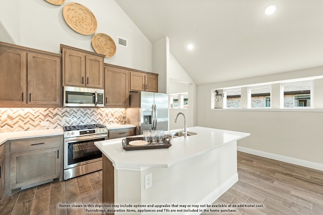 kitchen featuring sink, hardwood / wood-style flooring, a center island with sink, high vaulted ceiling, and appliances with stainless steel finishes