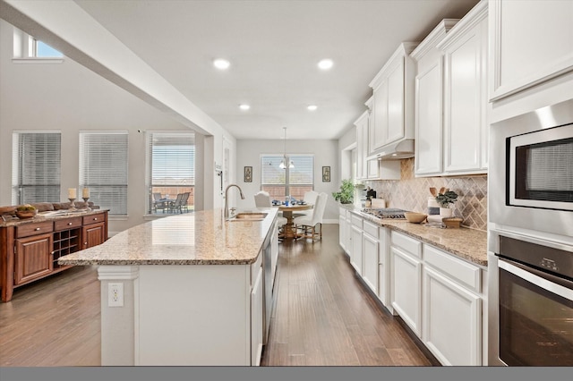 kitchen with decorative light fixtures, white cabinetry, stainless steel appliances, tasteful backsplash, and a kitchen island with sink