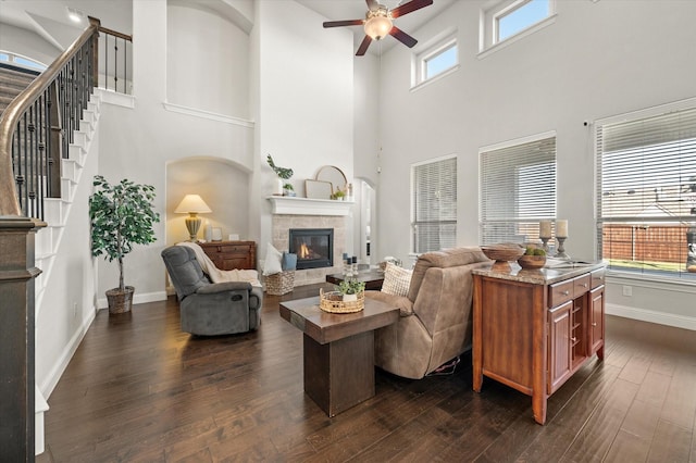 living room featuring a towering ceiling, ceiling fan, a tile fireplace, and dark hardwood / wood-style flooring