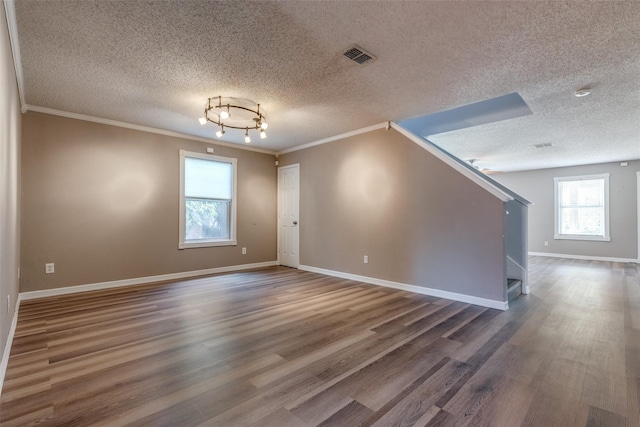 empty room featuring a textured ceiling, dark hardwood / wood-style flooring, ornamental molding, and a notable chandelier