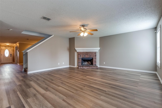 unfurnished living room with a fireplace, ceiling fan, wood-type flooring, and a textured ceiling