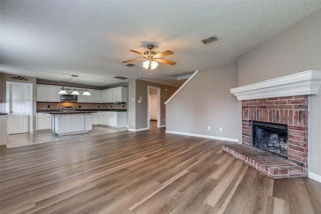 unfurnished living room with hardwood / wood-style flooring, ceiling fan, a textured ceiling, and a brick fireplace