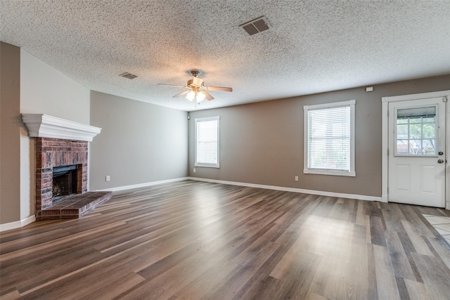 unfurnished living room featuring hardwood / wood-style floors, a textured ceiling, a brick fireplace, and plenty of natural light