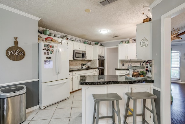 kitchen featuring white cabinets, a kitchen bar, stainless steel appliances, and ornamental molding