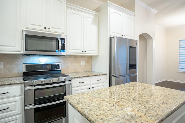kitchen with white cabinetry, light stone counters, ornamental molding, appliances with stainless steel finishes, and backsplash