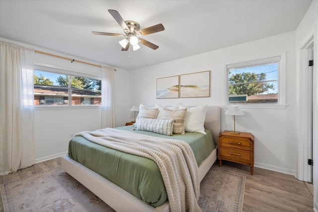 bedroom with ceiling fan, multiple windows, and light hardwood / wood-style flooring