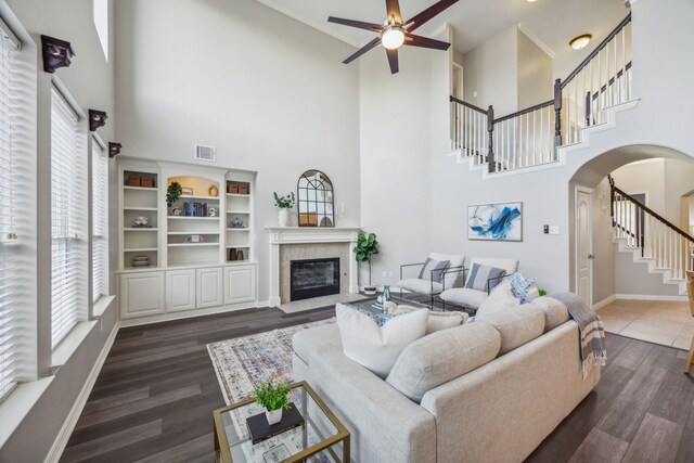 living room with dark hardwood / wood-style floors, ceiling fan, a towering ceiling, and a fireplace