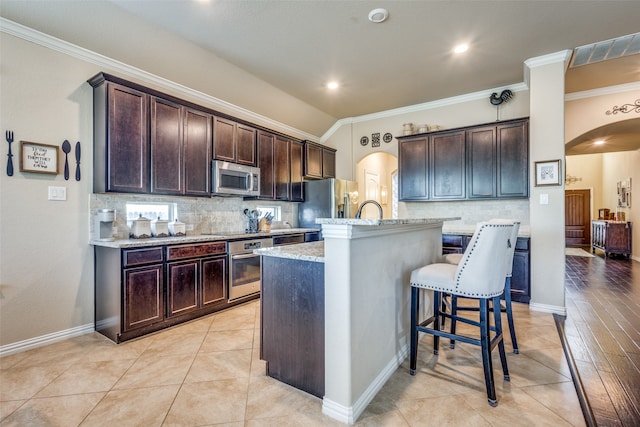 kitchen featuring appliances with stainless steel finishes, light wood-type flooring, light stone counters, a breakfast bar, and an island with sink