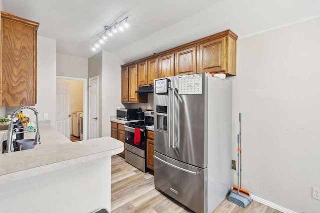 kitchen with track lighting, stainless steel appliances, sink, washing machine and dryer, and light hardwood / wood-style floors