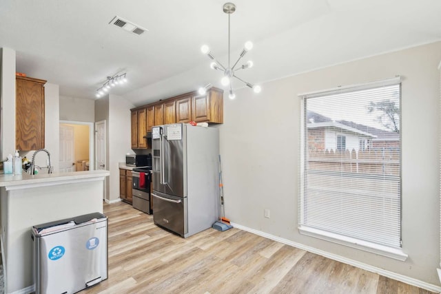 kitchen with appliances with stainless steel finishes, light wood-type flooring, sink, an inviting chandelier, and hanging light fixtures