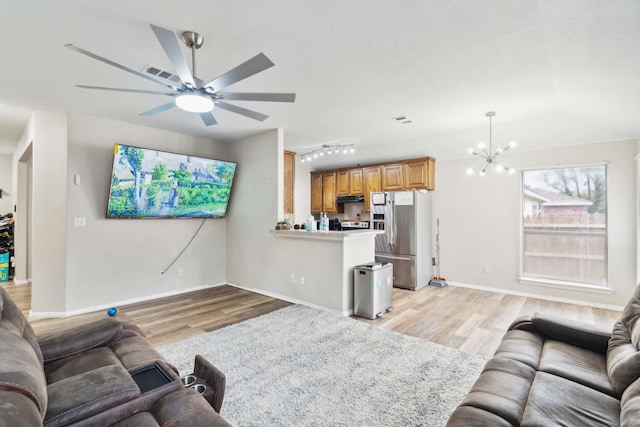 living room with ceiling fan with notable chandelier, rail lighting, and light hardwood / wood-style flooring