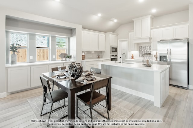 kitchen featuring backsplash, stainless steel appliances, vaulted ceiling, sink, and white cabinets