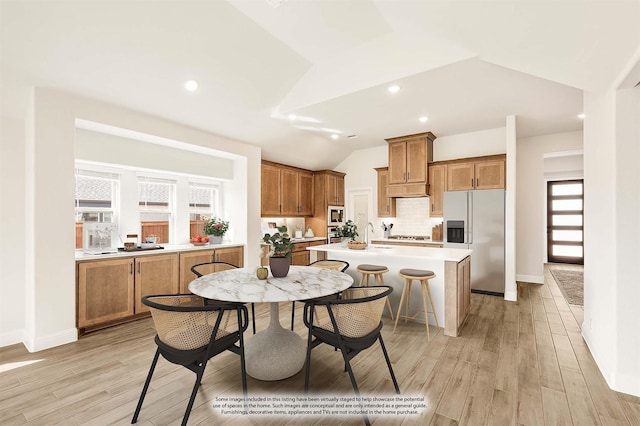 kitchen with a kitchen island with sink, stainless steel appliances, vaulted ceiling, light countertops, and brown cabinetry