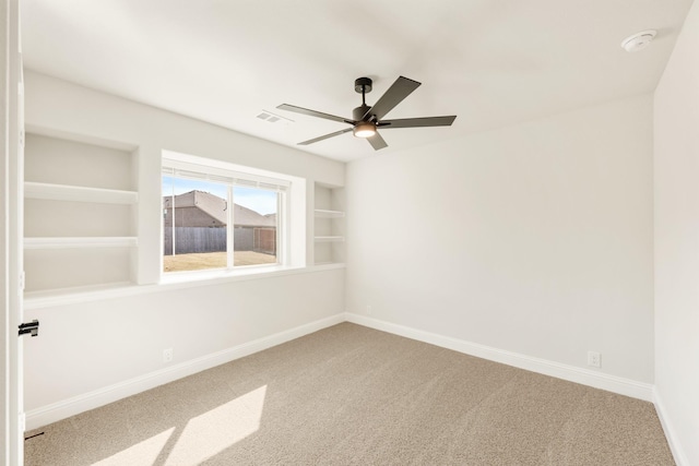 carpeted empty room with built in shelves, visible vents, baseboards, and a ceiling fan