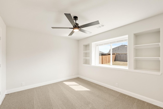 carpeted empty room featuring baseboards, a ceiling fan, visible vents, and built in features